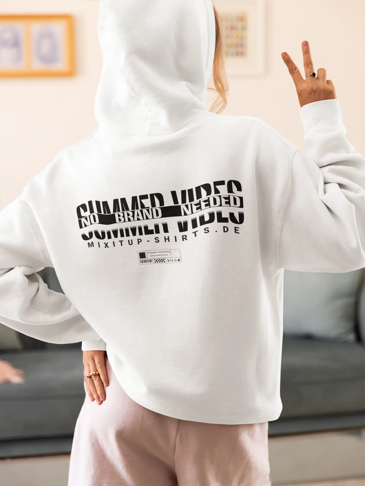Frau im weißen Unisex Hoodie mit großem schwarzen Backprint SUMMER VIBES und NO BRANDS NEEDED. Kollektionsbild für nachhaltige Mode.