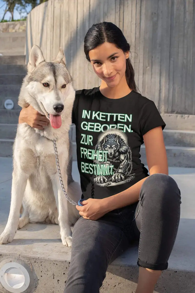 Schwarzes Oversized Streetwear T-Shirt mit großem Rückenprint: Ein muskulöser Wolf in schweren Eisenketten bricht aus der Gefangenschaft aus. Über dem Motiv steht der Text „IN KETTEN GEBOREN“ und darunter „ZUR FREIHEIT BESTIMMT“ in weißer Vintage-Schrift